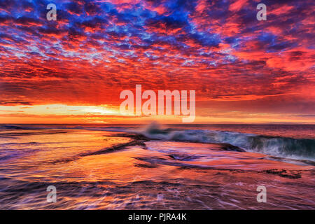 Couleurs vives aube sur le plateau de grès à Mona Vale beach de l'Australie, Sydney, avec des vagues de l'océan Pacifique s'attaquer à la côte. Banque D'Images