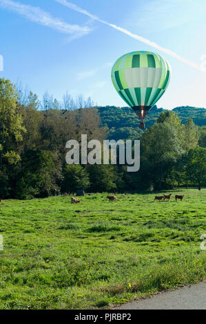 Ballon à air chaud vert grimpant sur la vallée de l'Aveyron et le village médiéval de Najac, Aveyron, Occitanie, France, l'Europe à l'automne Banque D'Images