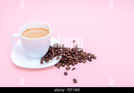 Grains de café torréfié dispersés dans une tasse sur un fond rose, copiez l'espace. Banque D'Images