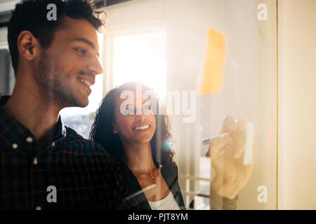 Collègues de bureau d'affaires de discuter des idées et des plans sur un verre transparent de sélection. Business couple écrit le post-it collé sur le verre conseil en o Banque D'Images