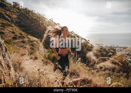 entraînement femme sportive pour course de cross-country sur un sentier de montagne. Femelle courant sur un sentier rocheux à flanc de colline. Banque D'Images