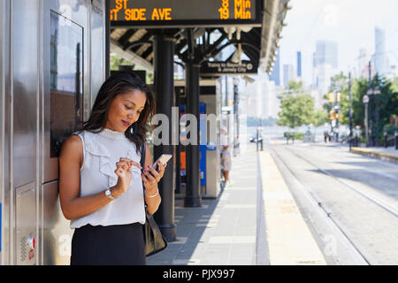 Businesswoman using cellphone par ticket machine Banque D'Images