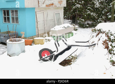 Chalet jardin dans la neige, brouette et remise. L'heure d'hiver. Banque D'Images