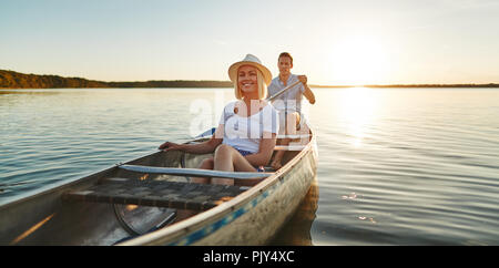 Souriante jeune femme assise avec son petit ami dans un canoë sur un lac encore sur un après-midi de fin d'été Banque D'Images