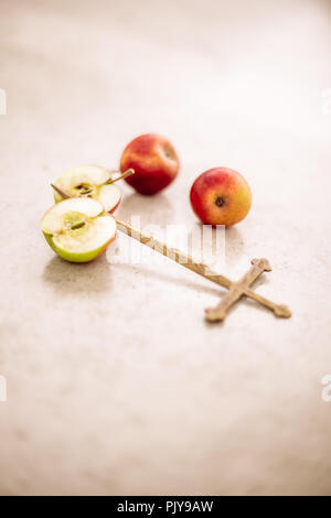 Nature morte scène conceptuelle abstraite d'une croix en métal décorée entourée de pommes entières et tranchées Banque D'Images