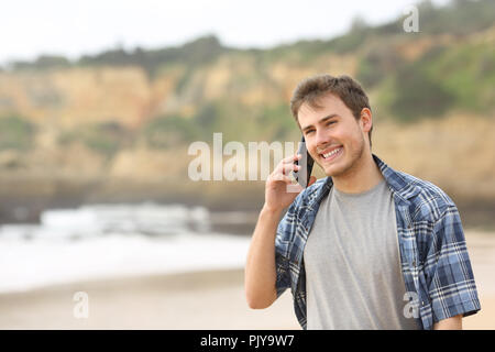 Teenage guy talking on mobile phone marche sur la plage Banque D'Images