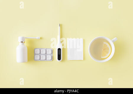 Le traitement du rhume et de la grippe. Comprimés, spray gorge, thermomètre, tasse de thé au citron simple sur fond jaune. La thérapie de soins de santé. Télévision lay, top vi Banque D'Images
