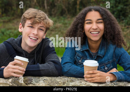 Mixed Race groupe de deux adolescents enfants heureux, African American girl, caucasian boy s'appuyant sur un mur de rire et de boire du café à emporter ensemble Banque D'Images