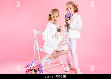 Portrait de deux jeunes filles sur un fond de poudre. Une fille dans une robe est assis sur une chaise, et l'autre en tailleur pantalon se trouve à côté d'elle. Banque D'Images