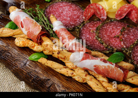 Pour des collations antipasti gressins enveloppée avec prosciutto (Grissini) avec le salami sur la surface en bois Banque D'Images