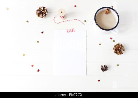 Composition décorative de Noël. Carte de voeux vierge, la liste de souhaits maquette des lieux. Image de pommes de pin, des bâtons de cannelle, des confettis scintillants des étoiles et du café sur la table en bois blanc. Mise à plat, vue du dessus. Banque D'Images