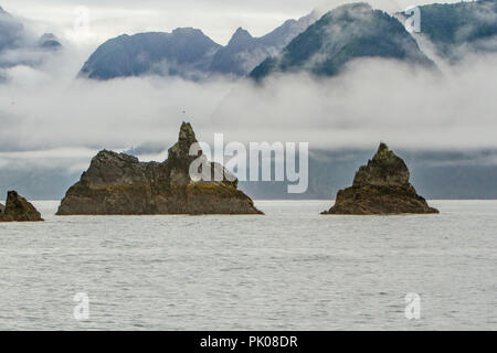 Chiswell Islands, situé dans la péninsule de Kenai, Alaska, USA. Deux formations de roche pinnacle dans l'eau avec des nuages et des collines vertes dans l'arrière-plan. Banque D'Images