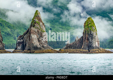 Chiswell Islands, situé dans la péninsule de Kenai, Alaska, USA. Deux formations de roche pinnacle dans l'eau avec des nuages et des collines vertes dans l'arrière-plan. Banque D'Images