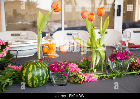 La table du déjeuner avec affichage floral de jolies fleurs aux couleurs orange et rose arrangements rougeâtre en premier plan avec une pastèque ronde & raisins Banque D'Images