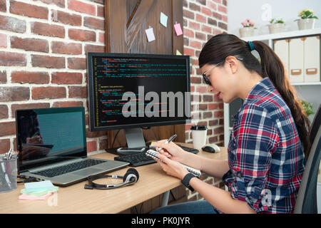 Les jeunes filles de programmeur et de l'écriture quelque chose vers le bas sur sa note. Banque D'Images