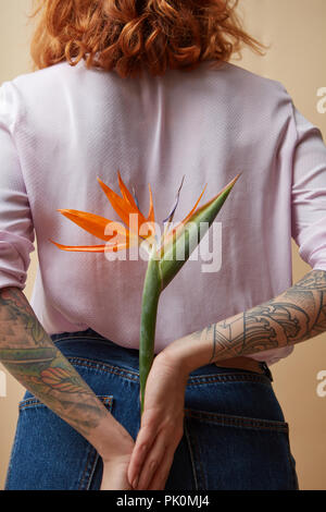 Girl in the pink shirt holding Flowers dans son tatouage les mains derrière le dos sur fond orange. Concept de vacances Banque D'Images