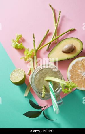 Les smoothies sains végétariens de légumes verts à feuilles vertes, tranches de citron, avocat, cocumber et paille en plastique dans un bol en verre sur duotone Banque D'Images