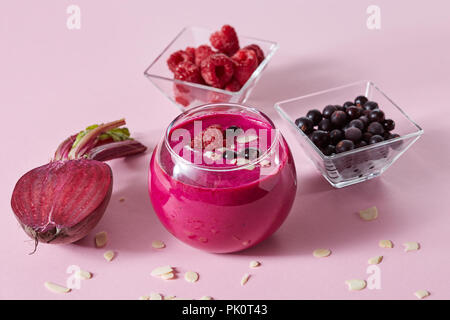 Les smoothies sains végétariens de fruits rouges et de betterave avec plaques d'amande dans une tasse en verre sur un fond de papier rose. Banque D'Images