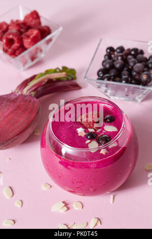 Les smoothies sains végétariens de fruits rouges et de betterave avec plaques d'amande dans une tasse en verre sur un fond de papier rose. Banque D'Images