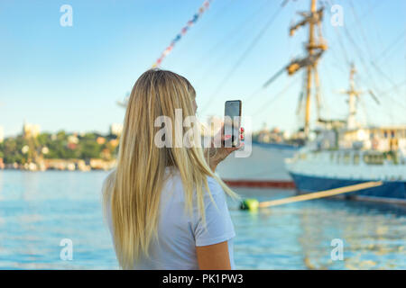 Une fille avec de longs cheveux blonds se tient en retrait et prend des photos de voiliers. Banque D'Images