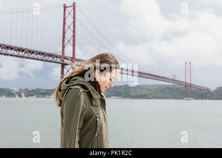 Une belle jeune fille seule promenades le long de la rive près du pont à Lisbonne. La solitude et les rêves. Banque D'Images