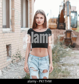 Belle fille de jean déchiré sur un chantier de construction près de l'excavateur. Banque D'Images