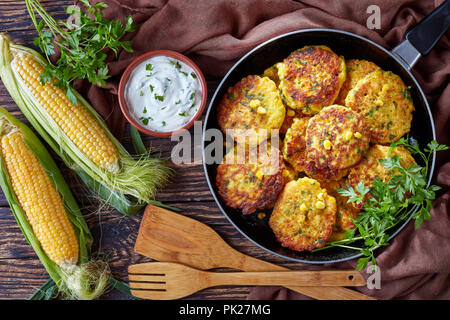 Beignets de maïs dans une poêle avec sauce trempette au yogourt et les épis de maïs sucré frais sur une vieille table de cuisine en bois, vue de dessus, flatlay Banque D'Images