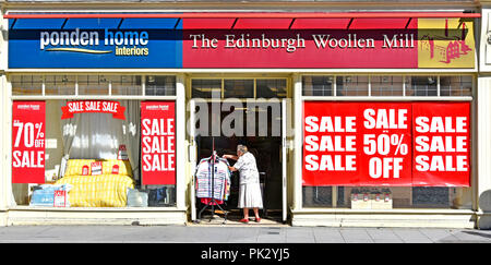 Old Lady shopping à tringle dans l'entrée de l'usine de laine Édimbourg high street magasin de vêtements au détail Vente posters shop UK Essex Brentwood vitre avant Banque D'Images