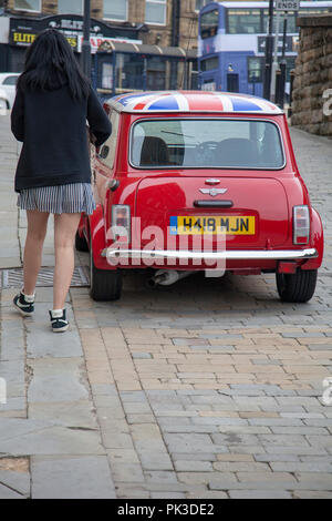 Vue arrière d'une Mini Cooper rouge avec un toit Union Jack avec une mini-jupe fille qui marche en voiture. Une version John Cooper de la voiture garée dans une rue Banque D'Images