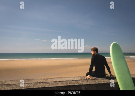 Surfer avec une planche de surf assis sur mur Banque D'Images