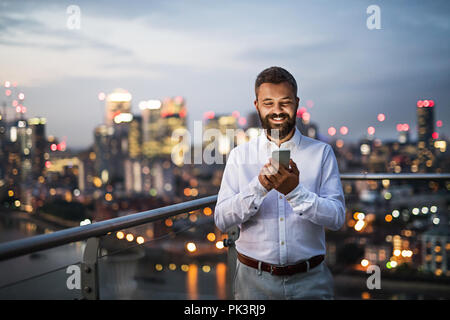 Un homme d'affaires avec le smartphone contre permanent nuit panorama de Londres. Banque D'Images