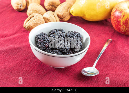 Les mûres et délicieux de fruits noirs mûrs et de grenat rouge. Dans un bol blanc et rouge sur fond blanc. À la pomme, l'abricot, de citron et de noix Banque D'Images