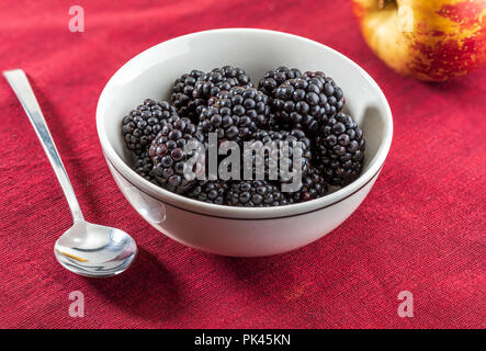 Les mûres et délicieux de fruits noirs mûrs et de grenat rouge. Dans un bol blanc et rouge sur fond blanc. Avec apple et rouge. Banque D'Images