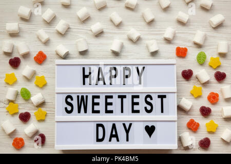 Conseil moderne avec texte 'Happy Sweetest Day' mot et candy sur la surface en bois blanc, vue du dessus. À partir de ci-dessus, mise à plat, les frais généraux. Banque D'Images