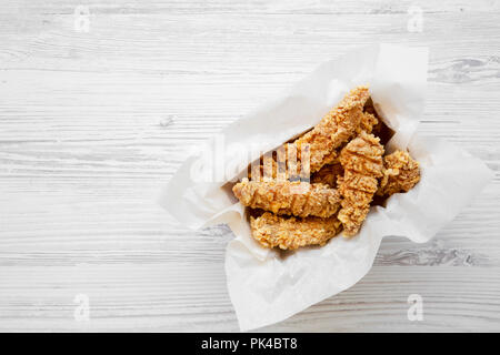 Doigts de poulet dans du papier fort sur une table en bois blanc, vue du dessus. Mise à plat, à partir de ci-dessus, les frais généraux. Copier l'espace. Banque D'Images