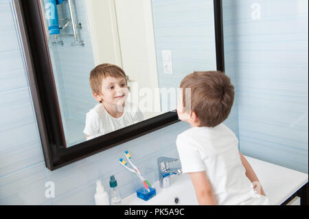 Mignon petit enfant caucasien sain à regarder lui-même dans un miroir dans salle de bains bleue Banque D'Images