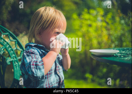 Un petit enfant est assis dans un jardin, c'est boire du café tasse Banque D'Images