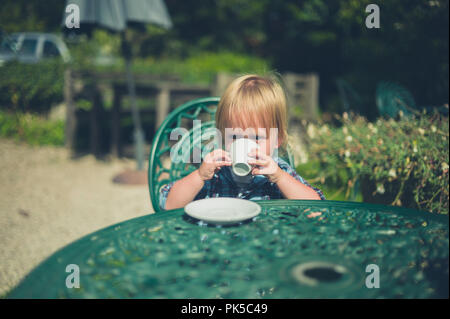 Un petit enfant est assis dans un jardin, c'est boire du café tasse Banque D'Images