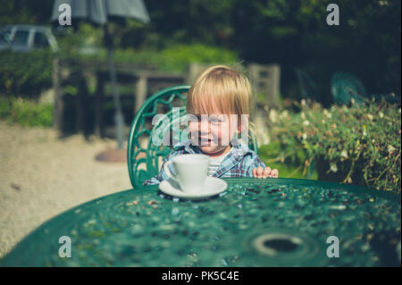 Un petit enfant est assis dans un jardin, c'est boire du café tasse Banque D'Images