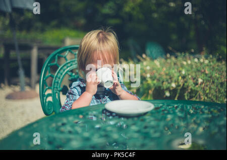 Un petit enfant est assis dans un jardin, c'est boire du café tasse Banque D'Images