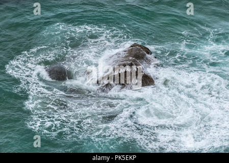 Marée montante, tourbillonnant autour d'un gros rocher dans la mer. Banque D'Images