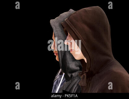 Deux adolescents en difficulté avec capuche noir debout à côté de l'autre en profil isolé sur fond noir Banque D'Images