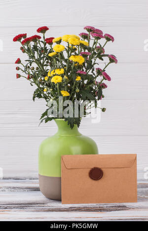 Fleurs dans un vase et mail avec sceau en cire stamp. Rouge, jaune et rose fleurs de chrysanthème. Fond de bois blanc. Banque D'Images