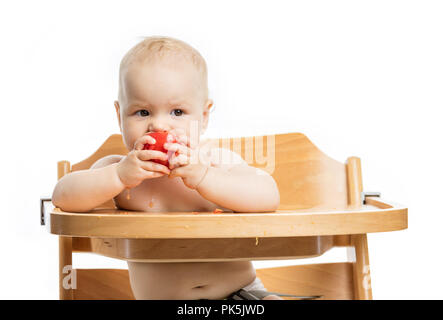 Cute baby girl eating tomato tout en étant assis sur une chaise haute sur fond blanc Banque D'Images