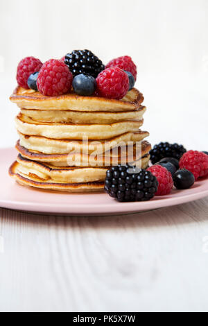 Crêpes aux fruits rouges sur une plaque rose sur fond de bois blanc, vue de côté. Close-up. Banque D'Images