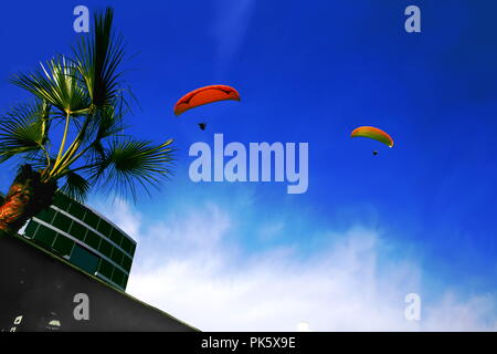 Deux parapentes qui volent dans le ciel bleu de la ville de Lima, Pérou, entre une masse de nuages et d'un bâtiment, d'un palmier d'un côté.Faible angle Banque D'Images