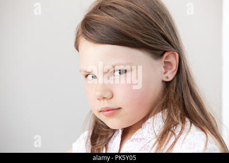 Face portrait de petite fille blonde sérieuse, photo en gros plan sur fond de mur blanc Banque D'Images