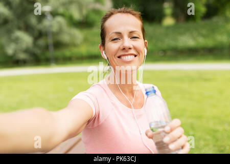 Femme dans les écouteurs et la prise d'eau en selfies park Banque D'Images