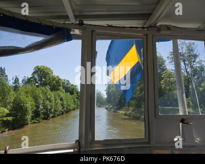 Le Göta kanal, croisière en bateau le long d'un cours d'eau idylliques en Suède vue du drapeau suédois et les paysages alentours, à partir de l'arrière du bateau à passagers Sandön Banque D'Images