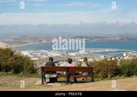 Trois personnes sur une journée ensoleillée assis sur un banc, sur l'Île de Portland à Portland au port. Dorset England UK GO Banque D'Images